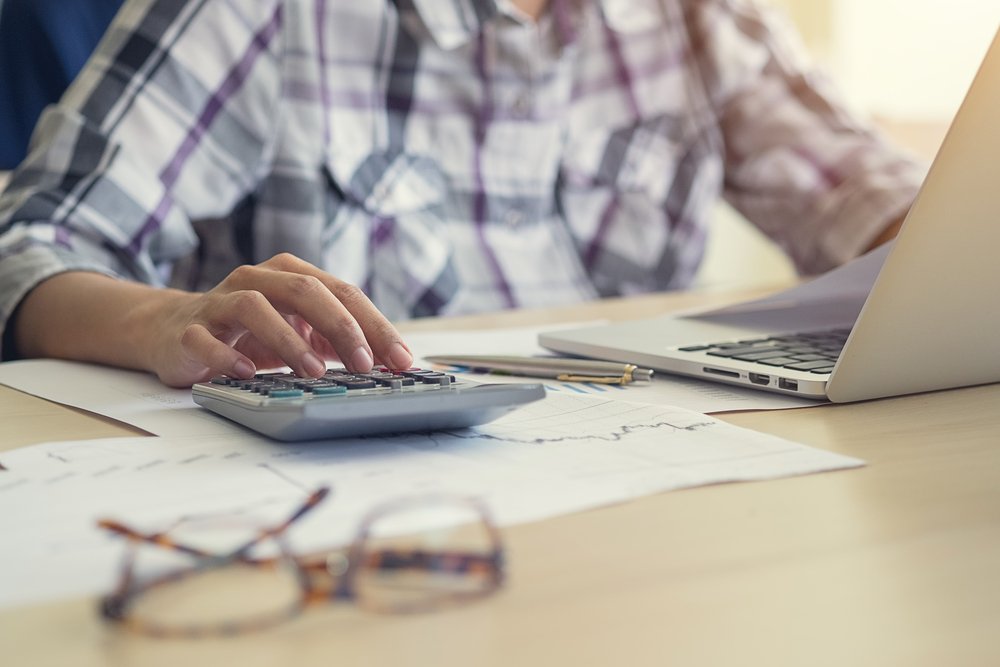 person calculating currency conversion manually with calculator and notebook